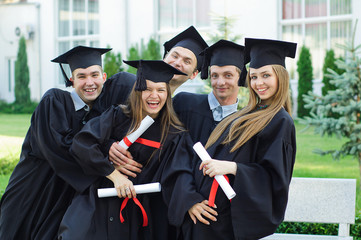 Group of laughing graduates with diplomas in their hands