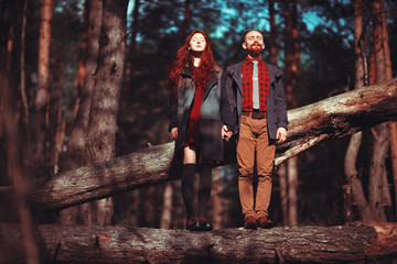 Fototapeta premium The red-haired guy with a beard and curly red-haired girl on the background of fabulous scenery of nature. Beautiful loving couple on a walk in the woods.