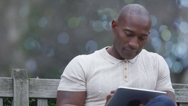  Smiling casual man looking at computer tablet in urban park area
