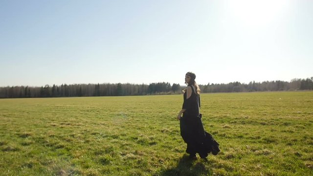 Beautiful girl in long black dress walks on field 