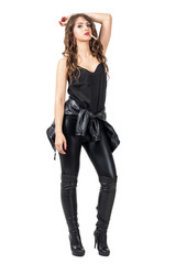 Sensual fashion model in leather clothes smoking cigarettes and resting arm on her head. Full body length portrait isolated over white studio background.