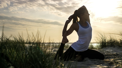 Young woman in a mermaid yoga pose on a sandy beach at sunset