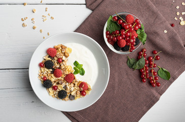 Healthy breakfast of two bowls, one with yogurt, muesli, raspberry and cherries, the other with mixed fruits on a background of violet tablecloth and white table