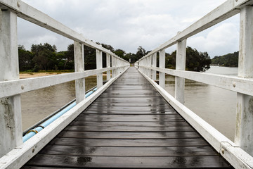 Fototapeta na wymiar White timber pedestrian bridge crossing on an overcast and drizzly day - no people