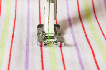 Foot of the sewing machine close-up on a striped cloth.