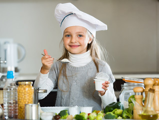 Little girl tasting fresh yoghurt in kitchen and smiling