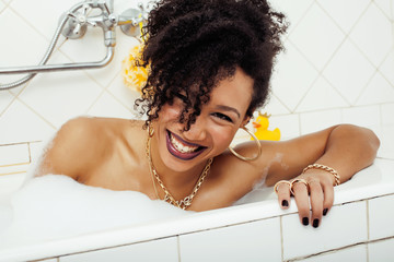 young afro-american teen girl laying in bath with foam, wearing swag jewelry flawless, making...