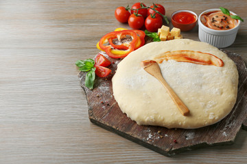 Fresh dough prepared for pizza with tomatoes and sliced pepper on a wooden board, close up