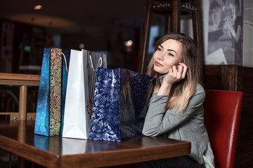Beautiful girl sitting at a table in a cafe talking on a cell phone and consider your purchase. Fashion Shopping lady Portrait. Beauty Woman with Shopping Bags in Shopping Mall. Shopper. 