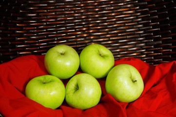 Vintage look of Green apples on red fabric with brown basket in background 