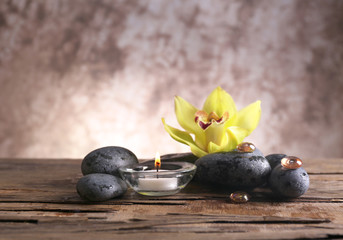 Fototapeta na wymiar Spa still life with stones, flower and candlelight on blurred pastel background