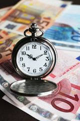 Time is money concept with pocket watch and euros bills closeup