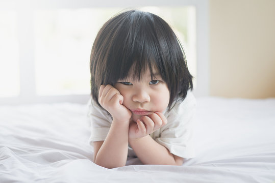 unhappy asian baby lying on white bed