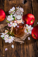 A bottle of apple cider vinegar (cider), fresh apples and apple-tree flowers on a wooden background. Country style.