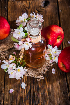 A bottle of apple cider vinegar (cider), fresh apples and apple-tree flowers on a wooden background. Country style.
