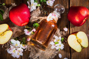 A bottle of apple cider vinegar (cider), fresh apples and apple-tree flowers on a wooden...