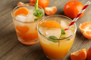 Two fresh delicious tangerine cocktails with ice, mint, straws and mandarins on the wooden table, close up