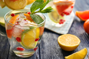 Refreshing cocktail with ice, mint, pomegranate seeds and slices of fruits on wooden background