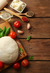 Pizza dough with tomatoes, olive oil, green basil and Mozzarella on wooden background