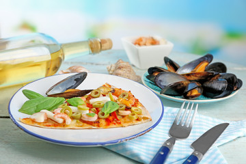 Pizza slice with seafood, red pepper, green olives and bottle of wine on wooden table