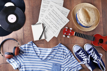 Guitar, headphones, music sheets and clothes on wooden surface, top view