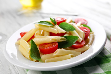 Plate of pasta with cherry tomatoes and basil leaves on table closeup