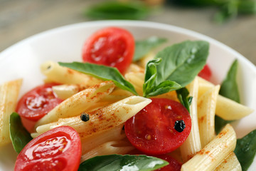 Plate of pasta with cherry tomatoes and basil leaves on table closeup