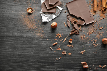 Pieces of chocolate with hazelnuts and cinnamon on black wooden background