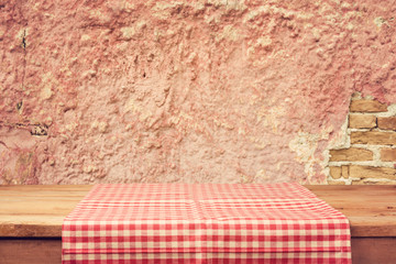 Empty wooden deck table with tablecloth over vintage wall background