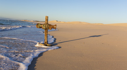 An old cross on sand dune next to the ocean with a calm sunrise