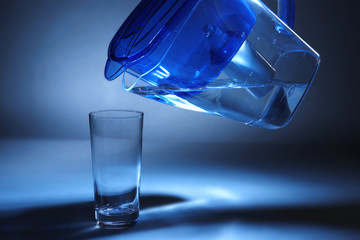 Filter jug pouring water in the glass, on dark background