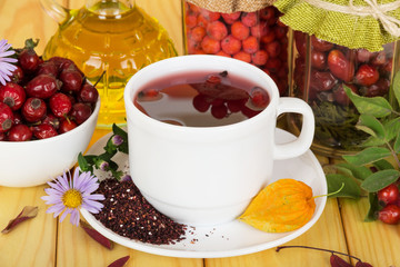 White cup with a drink from the berries of mountain ash and wild rose on  background  light wood.
