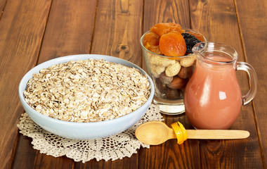 Bowl with oat flakes,  jug of juice, nuts and dried fruits on  background  dark wood.