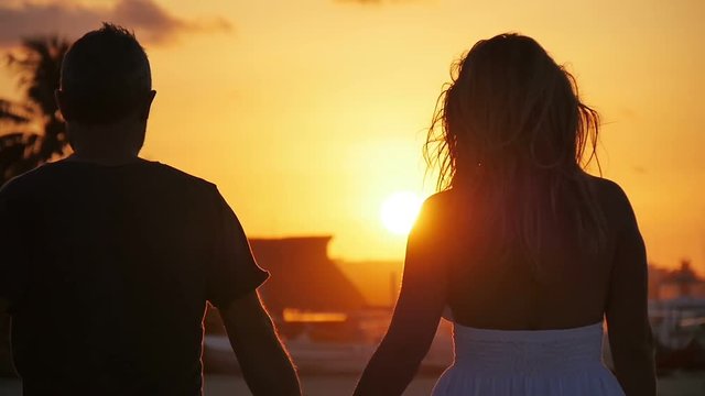 romantic couple walking away on the beach holding hands