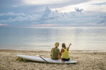 Happy couple with paddle board on the beach at sunset