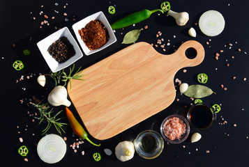 Food background. Empty cutting board and pepper, bay leaf, rosemary, onions, Himalayan salt, olive oil, soy sauce on a black background. The template for displaying products