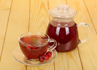 Jug and cup of rosehip drink on the background  light wood.
