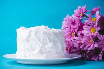 White creamy cake with flowers on the blue wooden background