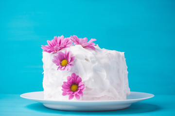 White creamy cake with flowers on the blue wooden background
