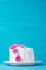 White creamy cake with flowers on the blue wooden background