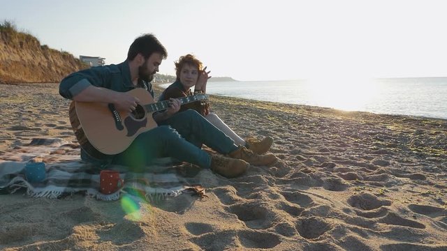 Young loving couple playing guitar on the beach, slow motion