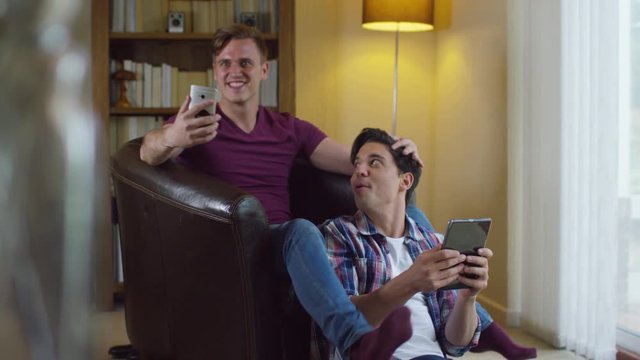  Attractive young gay couple relaxing at home, talking and using technology