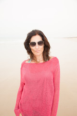 portrait brunette vacation pretty woman with sunglasses, red knitted sweater looking on sand with...