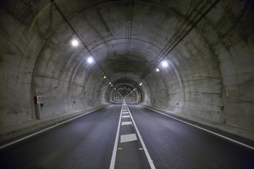 Fototapeta premium landscape straight grey lonely road tunnel with two lanes, white painting dividing lines in asphalt and light, in Spain Europe
