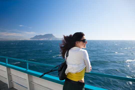 woman, white and yellow clothes, leaning on boat railing in ferry in Mediterranean sea Strait of Gibraltar with the Rock in the background, in Cadiz, Andalusia, Spain, Europe
