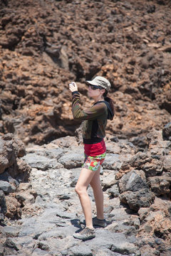 brunette woman with cap, green and red shirt with camera in volcanic nature as photographer taking photo picture, in Teide Volcano mountain, Tenerife, Canary Islands, Spain, Europe