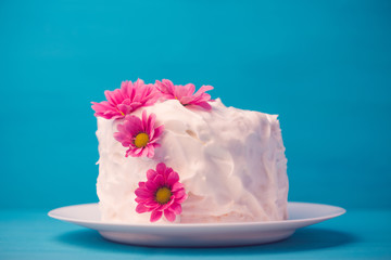 White creamy cake with flowers on the blue wooden background. Shallow depth of field. Toned image.