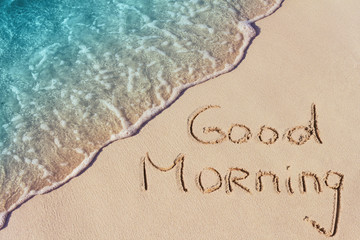 Goood Morning handwritten on sandy beach with  soft wave of ocean on background
