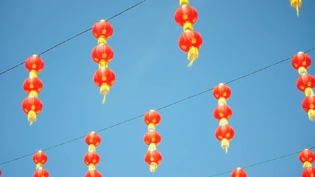 Red Chinese lanterns moving slowly against blue sky with soft breeze