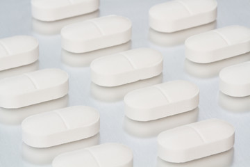 Rows of tablets or pills lined up in rows on a silver background.